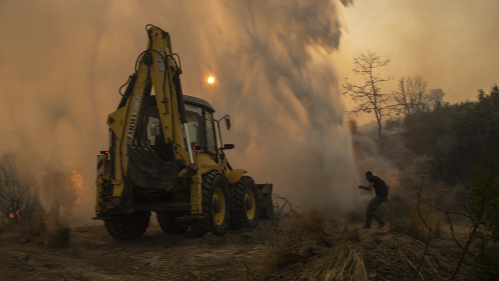 A bulldozer opens fire break as a local tries to avoid the water thrown by helicopter in Gennadi village, on the Aegean Sea island of Rhodes, southeastern Greece, on Tuesday, July 25, 2023. A firefighting plane has crashed in southern Greece, killing both crew members, as authorities are battling fires across the country amid a return of heat wave temperatures. (AP Photo/Petros Giannakouris) XTS138