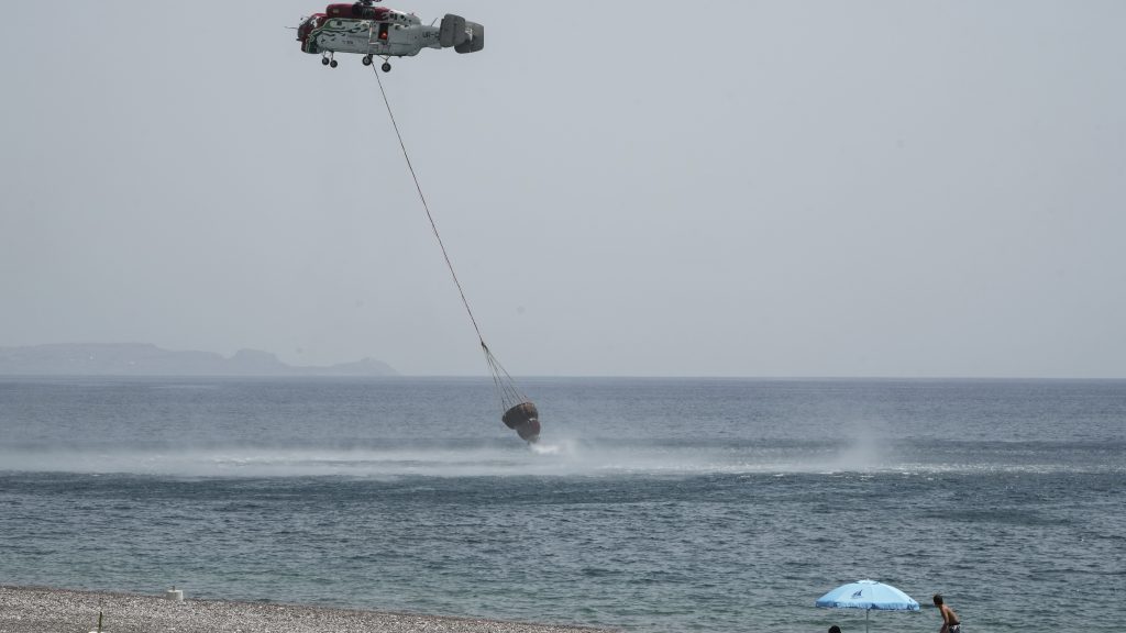 People watch from the beach an helicopter filling water from the sea during a wildfire, near Gennadi village, on the Aegean Sea island of Rhodes, southeastern Greece, on Thursday, July 27, 2023. The wildfires have raged across parts of the country during three successive Mediterranean heat waves over two weeks, leaving five people dead. (AP Photo/Petros Giannakouris) XTS111