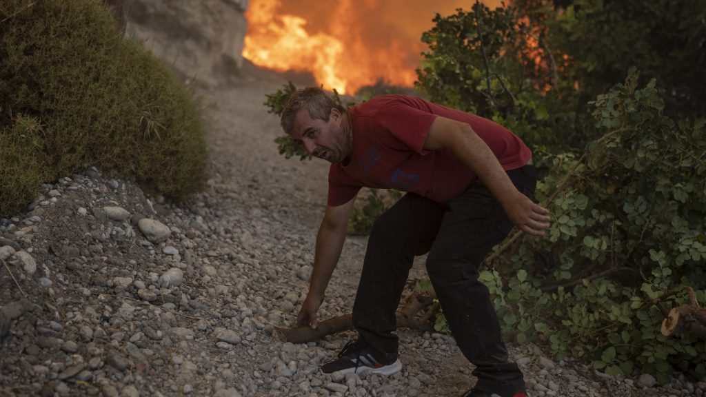 A local pulls a tree branch as a wildfire burns in Gennadi village, on the Aegean Sea island of Rhodes, southeastern Greece, on Tuesday, July 25, 2023. A firefighting plane has crashed in southern Greece, killing both crew members, as authorities are battling fires across the country amid a return of heat wave temperatures. (AP Photo/Petros Giannakouris) XTS143