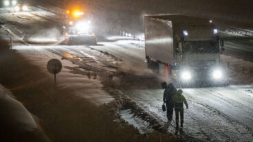 LANDSKRONA 2025-11-20 
Två man med spadar (!) och en traktor plogar då det är stopp i snö och hård vind på E6 norrut i backen upp mot Glumslöv utanför Landskrona på torsdagskvällen. Det har under varit stopp och stora problem med trafiken i snön och den hårda vinden på riksväg 17 och E6 vid Landskrona och Glumslöv under torsdagen. 
Foto: Johan Nilsson / TT / Kod 50090