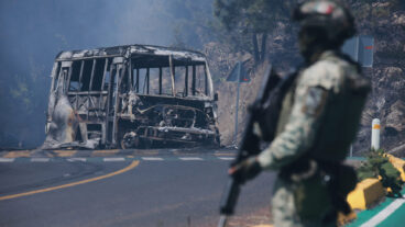 A soldier stands guard by a charred vehicle after it was set on fire, in Cointzio, Michoacán state, Mexico, Sunday, Feb. 22, 2026, following the death of the leader of the Jalisco New Generation Cartel, Nemesio Oseguera, known as "El Mencho." (AP Photo/Armando Solis)  XFLL108