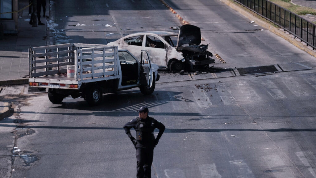 A police officer stands guard by a charred vehicle after it was set on fire, on a road in Guadalajara, Jalisco state, Mexico, Sunday, Feb. 22, 2026, after the death of the leader of the Jalisco New Generation Cartel, Nemesio Rubén Oseguera Cervantes, known as "El Mencho." (AP Photo/Alejandra Leyva) XFLL103
