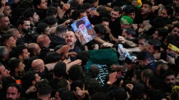 The coffin of the late Iranian Supreme Leader Ayatollah Ali Khamenei is carried through a tightly packed crowd as mourners jostle to reach and touch it outside the Imam Hussein Shrine in Karbala, Iraq, early Thursday, July 9, 2026. (AP Photo/Khalil Hamra)  XEM135